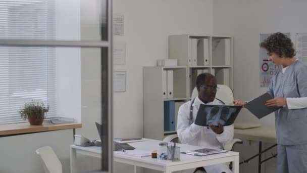 中位白种人医学专业人员与眼镜经验丰富的黑人男性医生就医疗室胸部X光扫描进行会诊 — 图库视频影像