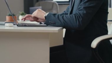 Erkek ofis çalışanının dizüstü bilgisayardaki işini bitiren, ayakta duran ve masadaki bilgisayar sandalyesini iten görüntüler.