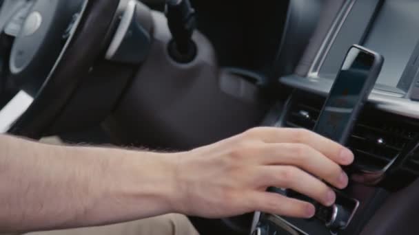 車の携帯電話ホルダーにスマートフォンをハンドステッキングし 運転中にそれを使用して 認識できないドライバーのサイドショットを閉じます — ストック動画