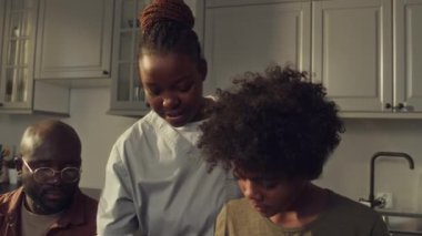 Afrika kökenli Amerikalı kadın hemşire, doktor üniforması, koca ve 10 yaşındaki oğlunun sabah mutfakta birlikte durup ekmek, jambon ve marullu salatadan sandviç yaparken yakın çekim.