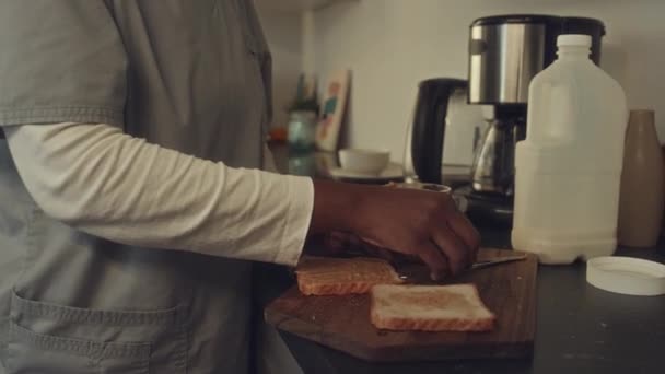 阳光明媚的早晨 身穿护士制服的非洲裔美国女卫生工作者站在厨房里 做花生酱三明治 放在儿子的背包里准备上学 — 图库视频影像