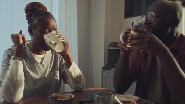 夫と息子とキッチンに座っている黒人の病院労働者のレンズフレアで中程度のクローズアップショット コーヒーを飲む 見ている キーを掴む Idバッジ さよならを言ってシフトを残す — ストック動画
