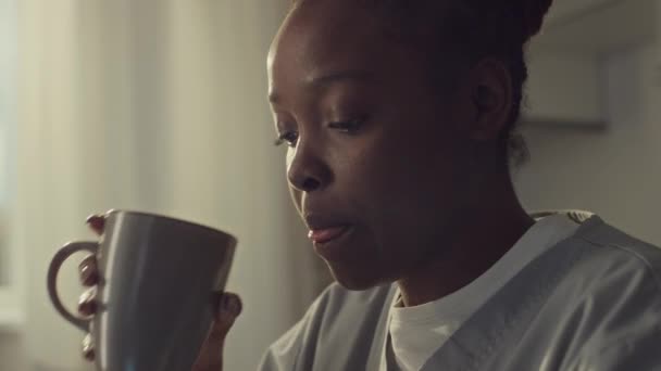 早上穿着医疗制服坐在厨房餐桌旁 吃三明治 喝茶或咖啡 并在换班前用智能手机输入信息的非洲裔美国女青年的特写镜头 — 图库视频影像