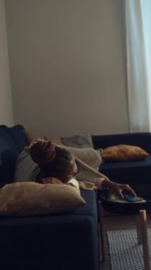 Üniformalı Afro-Amerikalı kadın doktorların evdeki kanepede uyuduğu, akıllı telefondaki çalar saatin öttüğü, kadının uyandığı ve işe gitmek için kalktığı dikey çekim.