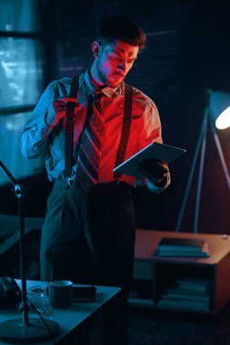 Genç ciddi erkek analist ya da iş şirketinin yöneticisi elinde tabletle karanlık ofisteki elektronik belgelere bakıyor.