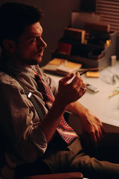 年轻疲惫的商人 手里拿着吸烟的香烟 坐在工作场所的镜头前休息时的侧影 — 图库照片