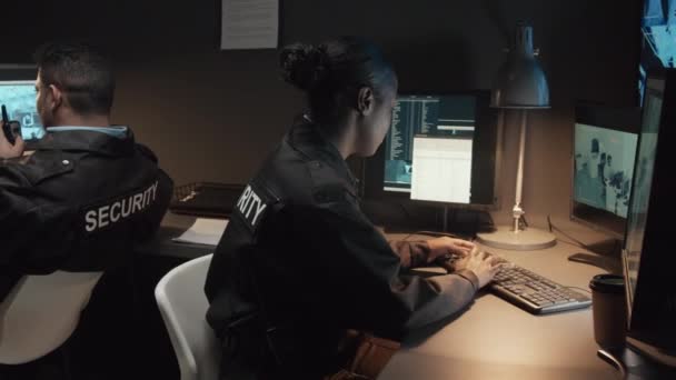 コンピュータと男性のBiracialの同僚で働く黒人女性警備員の中型ショット 監視室でCctvカメラを制御するウォルキー トーキーについて話す — ストック動画