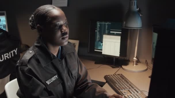 モニター上のCctvビデオ映像を制御するユニフォームで若いアフリカ系アメリカ人の警備員のチェストアップショットと監視室のウォルキー トーキーで話す — ストック動画