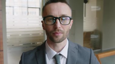 Kafkasyalı, gözlüklü ve resmi giysili bir yöneticinin modern ofis girişinde kameraya bakarken yakın plan portresi.