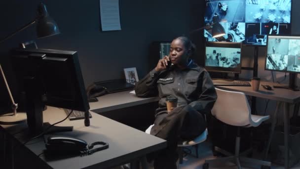 全片拍摄的年轻黑人女警一边接电话一边喝咖啡 一边看着监控室里有多个闭路电视镜头的监视器屏幕 — 图库视频影像
