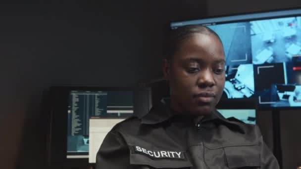 携帯電話を使用して制服を着た若い黒人女性警備員のズームアウトショットは 警備室で仕事中にCctvビデオ映像でスクリーンを見ていません — ストック動画