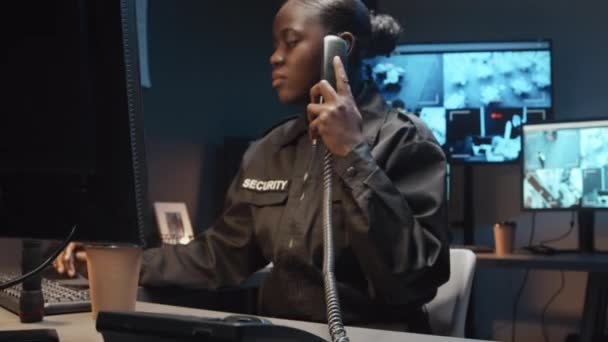 Cctvの映像の複数のスクリーンが付いている監視室の地上電話の黒い女性の警備員および答える仕事の呼出しの中型ショット — ストック動画