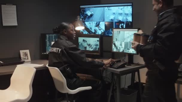 監視室でCctv映像を監視する女性黒人の同僚にランチブレイクのために軽食とコーヒーを持って来るBiracial男性警備員のミディアムショット — ストック動画