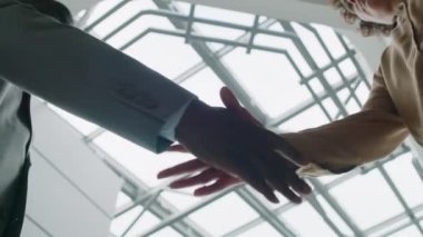 Aşırı düşük açılı, iki farklı kimliği belirsiz iş ortağının camdan çatıyla ofis salonunda el sıkışması.