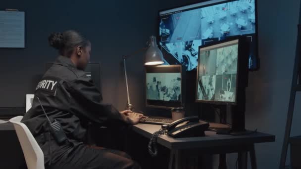 身穿黑色制服 面带微笑的年轻非裔美国卫兵控制闭路电视录像镜头 然后看着坐在监控室里的摄像机的画像 — 图库视频影像