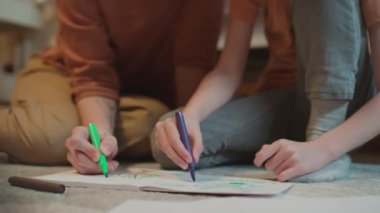 Seçici odak noktası, tanınmayan anne ve oğlunun yatak odasında oturup renkli resimler çizerken kalem kalem kullanmaları.