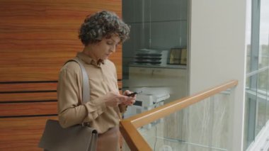 Kafkasyalı iş kadınının resmi kıyafetli orta yavaş portresi telefonda mesaj yolluyor ve sonra da ofisteki kameraya bakıyor.