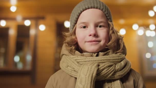 身穿卡其布贝尼和围巾 留着波浪般的头发 站在木屋外的男孩的中特写肖像 — 图库视频影像