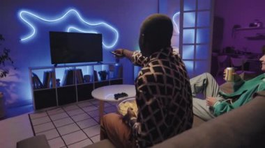 Koltukta oturan, elinde aperatifler ve sodayla televizyon seyreden ve neon ışıkları olan bir çiftin arkası.