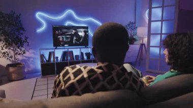 TV 'de mafya hakkında film seyreden ve modern odadaki neon ışıklı koltukta oturup tartışan çok ırklı çiftin arka planı.