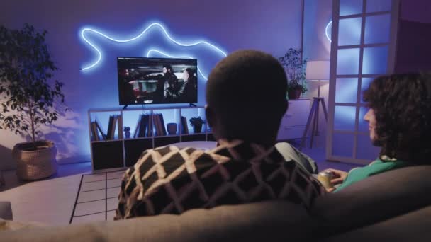 多民族夫妇在电视上观看黑手党电影的回顾 并在现代房间里与霓虹灯一起坐在沙发上讨论 — 图库视频影像