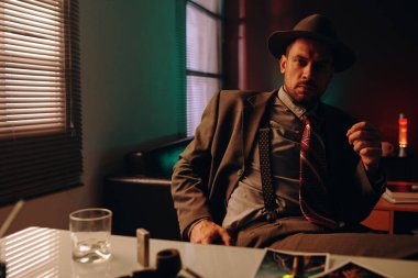 Formalite içinde kendine güveni tam bir adam karanlık ofiste iş yerinde oturuyor ve gece geç saatlere kadar çalışırken kameraya bakıyor.