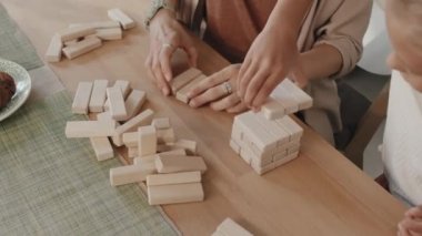 Anne ve kızının oyun için mutfak masasına ahşap blok kule inşa ederken yüksek açılı görüntüsü yavaşlıyor.