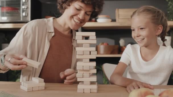 快乐的母亲和女儿坐在桌旁玩棋盘游戏 从塔台上移开方块 — 图库视频影像