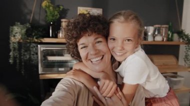 Mutfakta kızıyla fotoğraf çeken mutlu, beyaz bir kadının orta boy yavaş yavaş portresi.