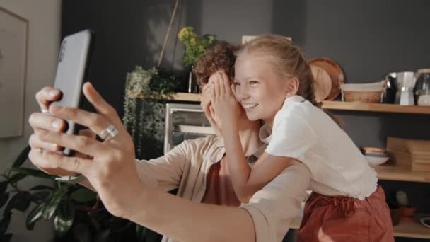快乐的母亲拿着智能手机 带着她可爱的十多岁的女儿自娱自乐 同时呆在家里 — 图库视频影像