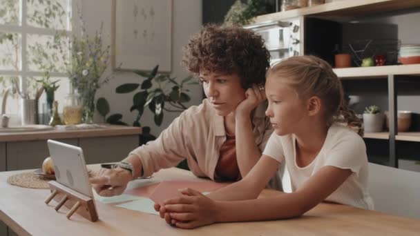 现代的年轻母亲们周末和女儿一起坐在厨房的餐桌旁 观看着数码平板电脑上的折纸教学 — 图库视频影像