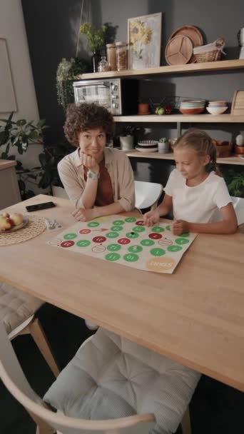 现代妈妈和她十多岁的女儿坐在餐桌旁玩棋盘游戏 然后邀请摄影师参加 — 图库视频影像