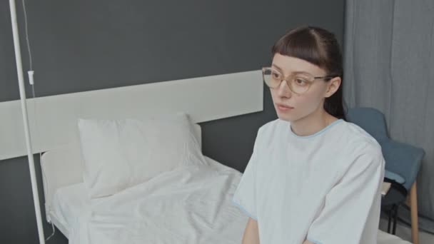 Средний Снимок Женщины Очках Больничном Платье Сидящей Палате Нервно Оглядываясь — стоковое видео