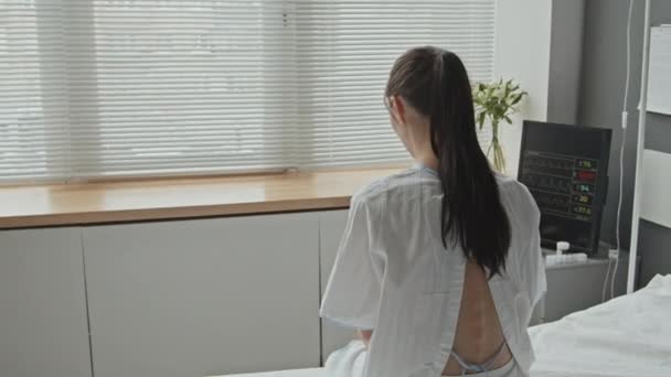 穿着医院长袍 身材苗条 一头黑发的女人 从后面看窗户 闭着百叶窗 — 图库视频影像