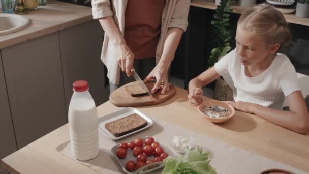 母亲切面包和做三明治 女儿吃含牛奶的麦片时拍摄的高角镜头 — 图库视频影像