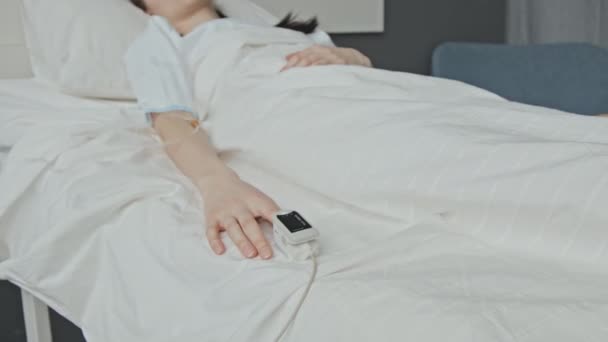 病院のベッドで意識不明に横たわる白人女性患者の選択的な焦点パンニングショット 静脈内線を介して液体を受信し 指先に脈拍の近似体を着用します — ストック動画
