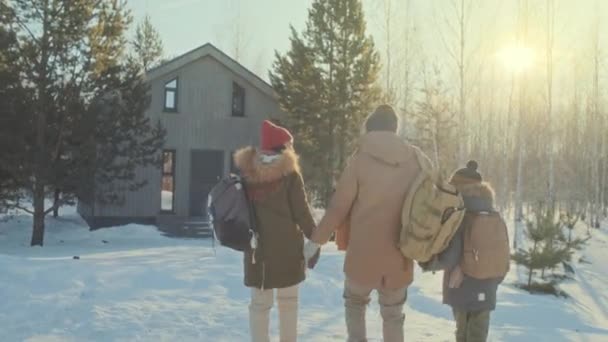 バックパックを身に着けている子供と家族のショットを追跡し 冬の日にコテージに向かって歩いている間に何かについて話す — ストック動画