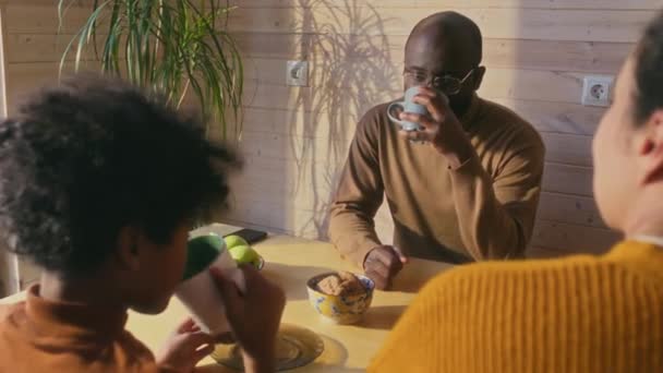アフリカ系アメリカ人の男性が 妻と息子が紅茶を飲んで クッキーを食べたり話したりする木製のテーブルに座っている選択的なフォーカスショット — ストック動画