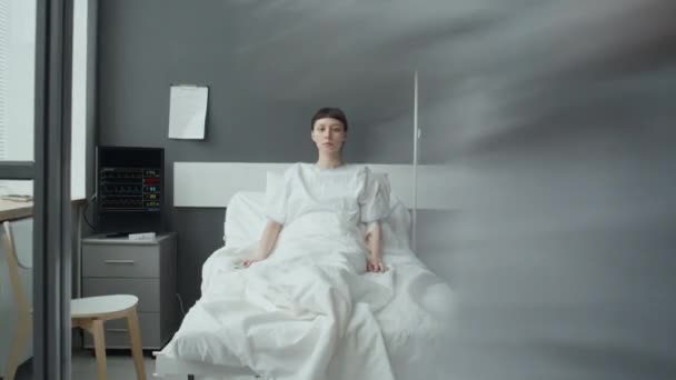 カメラを見ながらベッドに座っている白人女性の患者が 医師と看護師が彼女の世話をする時間の経過 — ストック動画