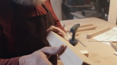 Atölyesinde beyaz sakallı bir marangoz kusurlarını araştırıyor.