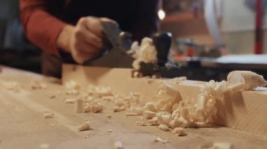 Tanımlanamayan marangoz arka planda çalışmaya devam ederken el uçağının ahşap talaşlarının seçici odaklı görüntüsü