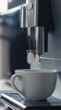 Dikey olarak, kahve makinesinin kahve fincanını kahve ya da kapuçino ile doldurması ve ofisteki tanınmayan bir ofis çalışanının bardak içmesi.