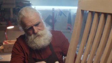 Kafkasyalı oduncunun beyaz renkli ahşap sandalyeyi zımpara kağıdıyla zımparalarken orta boy yakın çekimi.