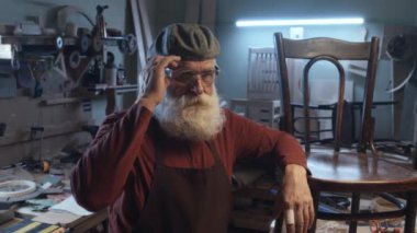 Sakallı yaşlı katılımcının portresi tahta sandalyeye yaslanmış kameraya bakarken güvenlik gözlüklerini çıkarıyor.