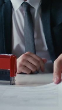 Takım elbiseli bir işadamının iş günlerinde belgelere kırmızı pul yapıştırırken dikey kesilen görüntüsü.