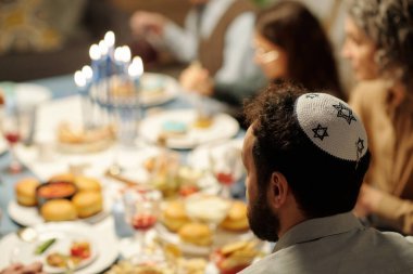 Yarmulke 'de, David' in yıldızlarıyla birlikte Hanuka yemeğinde servis edilen masanın önünde oturan olgun sakallı adamın yan görüntüsü.