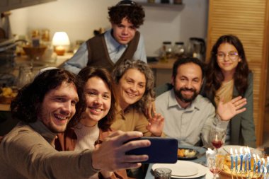 Akıllı telefonlu mutlu genç Yahudi bir adam büyük bir ailenin selfie 'sini çekiyor ya da Hanuka yemeğinde görüntülü sohbet ediyor.