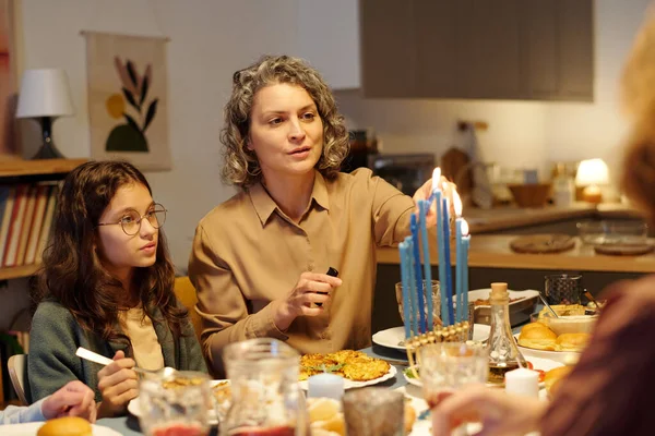 成熟的犹太妇女坐在女儿旁边准备晚饭时 在犹太烛台上点着蜡烛 — 图库照片