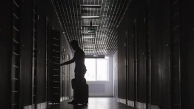 Uzun tek renkli erkek figürünün bavul ve el çantasıyla oteldeki odasını bulması.