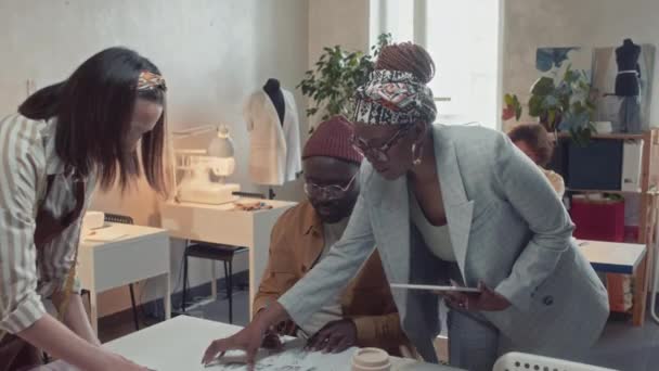 黒人男性ファッションデザイナーと白人女性テーラーのタブレットガイドと制御作業を持つ女性のアフリカ系アメリカ人テーラースタジオオーナーのミディアムショット — ストック動画